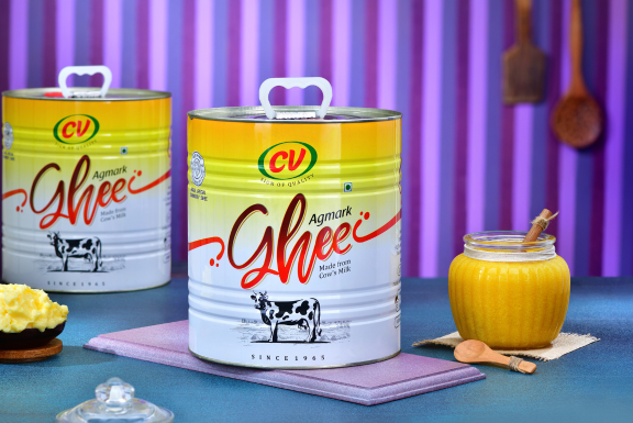 A butter jar and two tasty cv ghee cans are among the dairy items on display on a wooden platform.