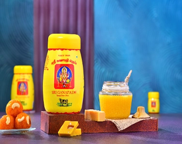 A woman in a white coat stands by the conveyor belt at the organic ghee manufacturer's dealership.